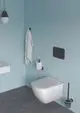 Weißer Wandtoilettensitz in modernem Badezimmer mit hellblauen Wänden. An der Wand hängen Handtuch und Toilettenpapierhalter in Schwarz. Ideal Standard Produkte sind sichtbar.